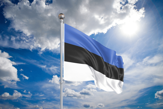 Lehviva Eesti lipp helesinise taeva ja valgete pilvede taustal.