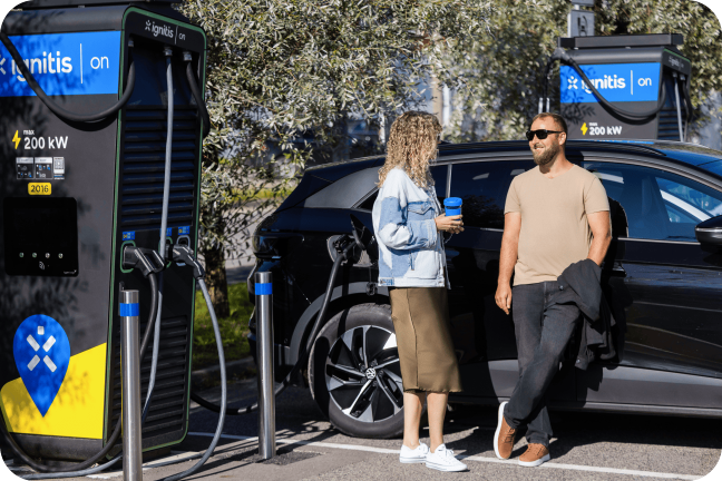 Naine joob kohvi ja vestleb mehega, samal ajal kui nende elektriauto laeb Ignitis ON-i kiirlaadimisjaamas.